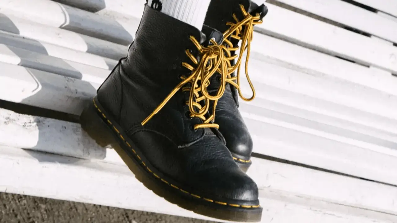 Schwarze Dr. Martens mit gelben Schnürsenkeln auf einer weißen Bank. Sie fallen eher groß aus, also lieber eine Nummer kleiner wählen.