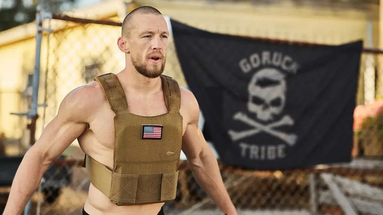 Mann mit Gewichtsweste und GORUCK-Flagge im Hintergrund, bereit für die Murph Challenge.