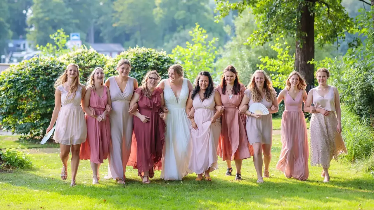 Brautjungfern in zarten Rosatönen, ein perfekter **dresscode hochzeit**, spazieren lachend über eine grüne Wiese.