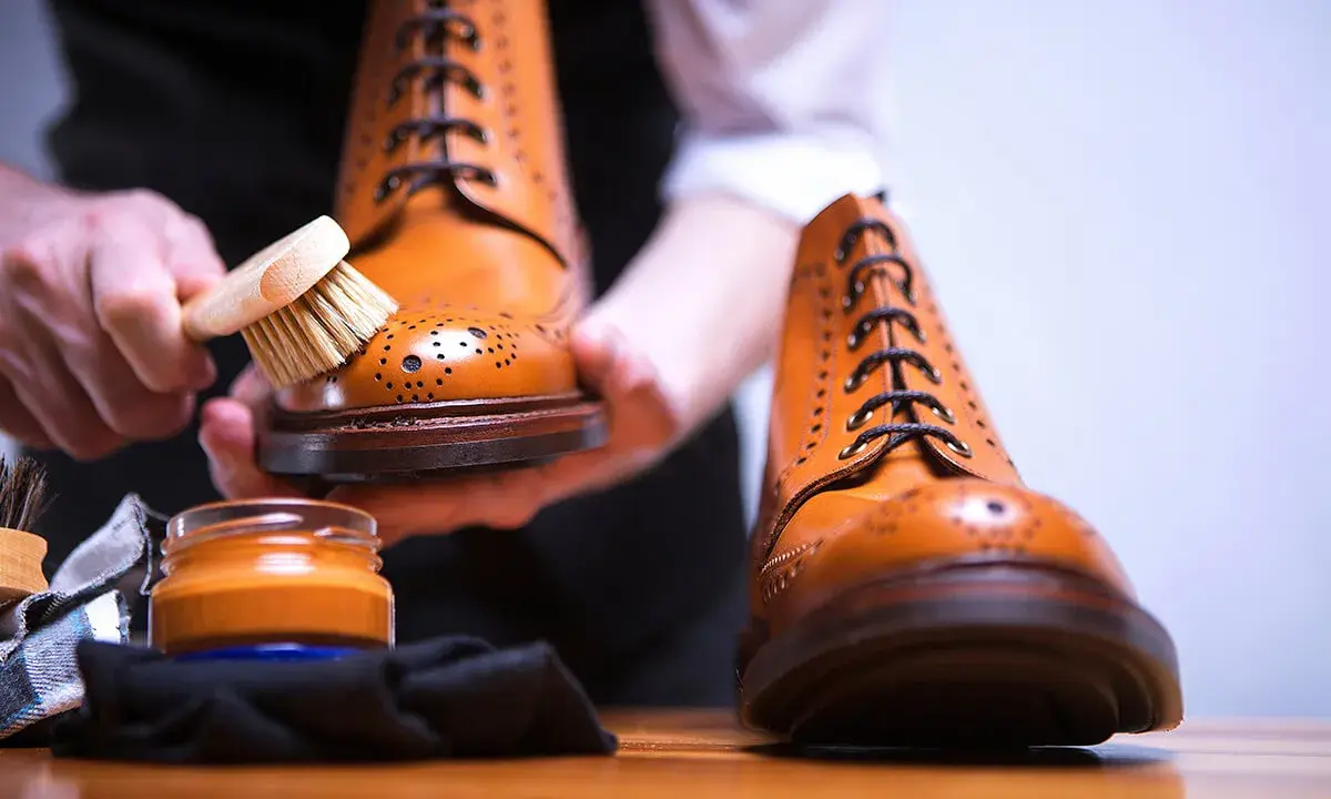 Hände bürsten braune Lederschuhe, um sie zu reinigen. Daneben steht eine Dose Schuhcreme.
