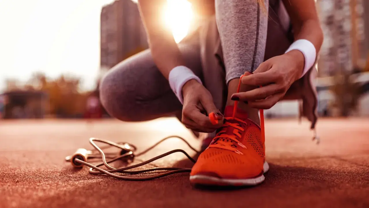 Sportlerin bindet ihre neuen, leuchtend orangen Laufschuhe ein. Die Sonne scheint, ein Springseil liegt bereit.