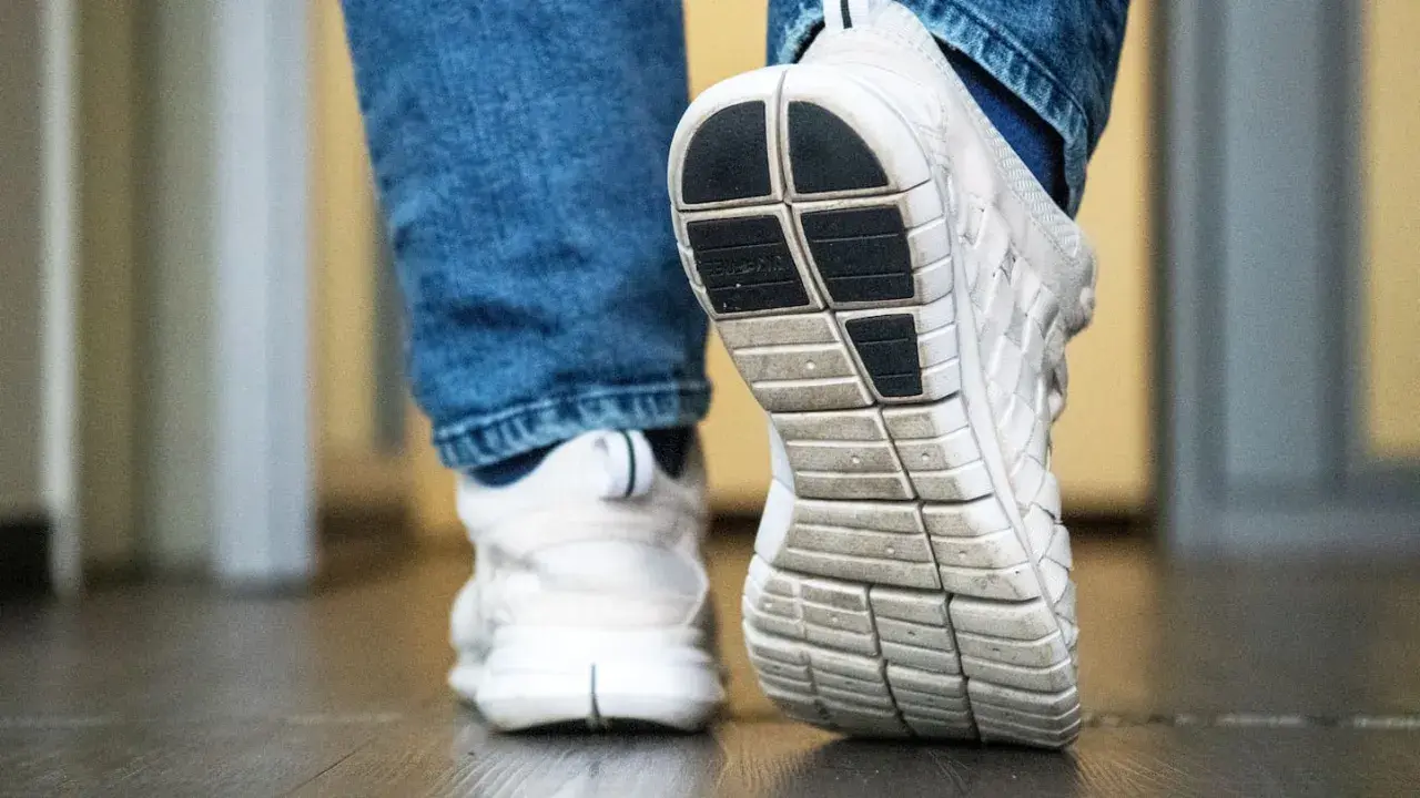Weiße Turnschuhe mit Jeans. Die Sohle der Schuhe quietschen auf dem Boden, als jemand einen Schritt macht.