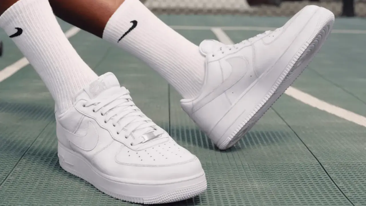 Weiße Nike Air Force 1 Sneaker mit schwarzen Socken auf einem grünen Untergrund. Perfekt zum Air Force 1 binden und loslegen.