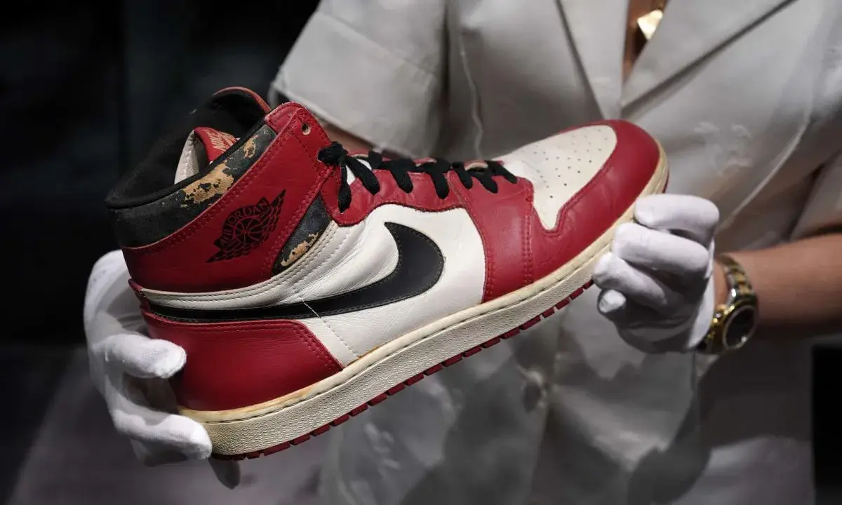 Ein ikonischer Air Jordan 1 Sneaker, der die Nike Air Jordan Geschichte verkörpert, wird von Händen in weißen Handschuhen präsentiert.