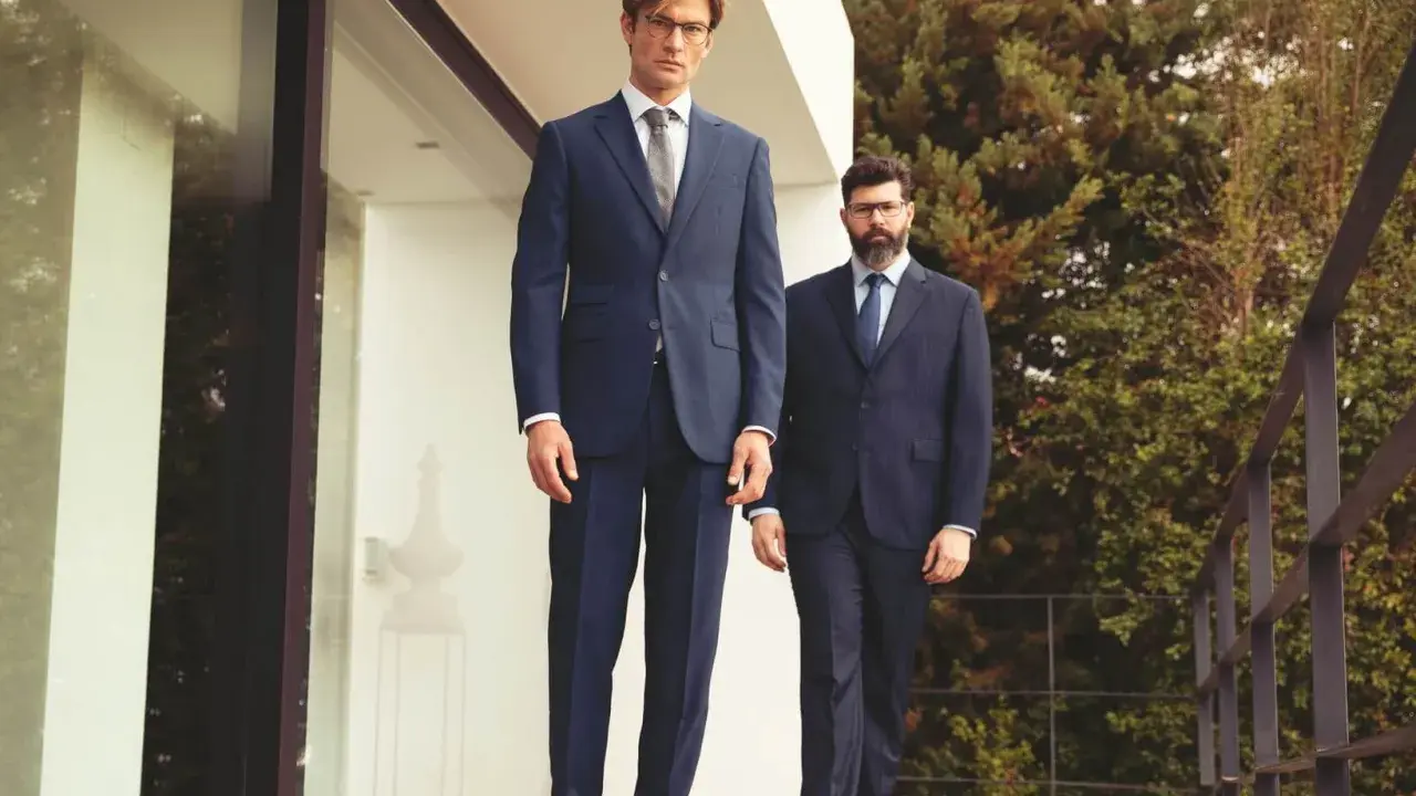 Zwei Männer in eleganten Anzügen, die aktuelle Anzug Trends verkörpern, stehen auf einer Holzterrasse vor einem modernen Gebäude.