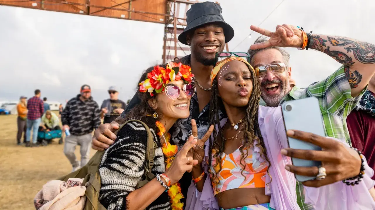 Bunte Outfits, Blumenkränze und Peace-Zeichen: So zieht man zu einem Rave an! Vier Freunde machen ein Selfie.