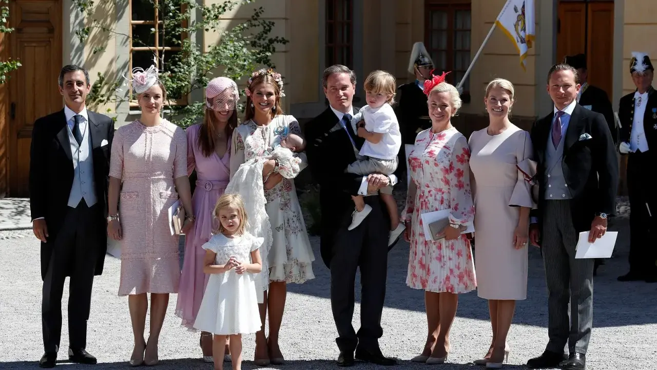 Familie in festlicher Kleidung, die überlegt, was anziehen zur Taufe. Ein Mann trägt ein Baby, Kinder und Frauen in eleganten Kleidern.
