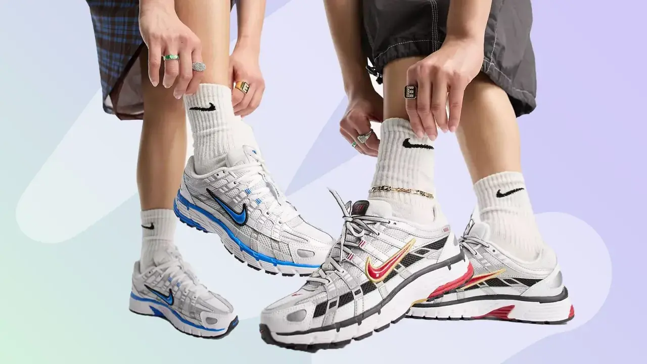 Zwei Paare Nike P-6000 Sneaker in Weiß mit blauen und roten Akzenten. Die Füße tragen weiße Socken mit Nike-Logo und auffälligen Schmuck.