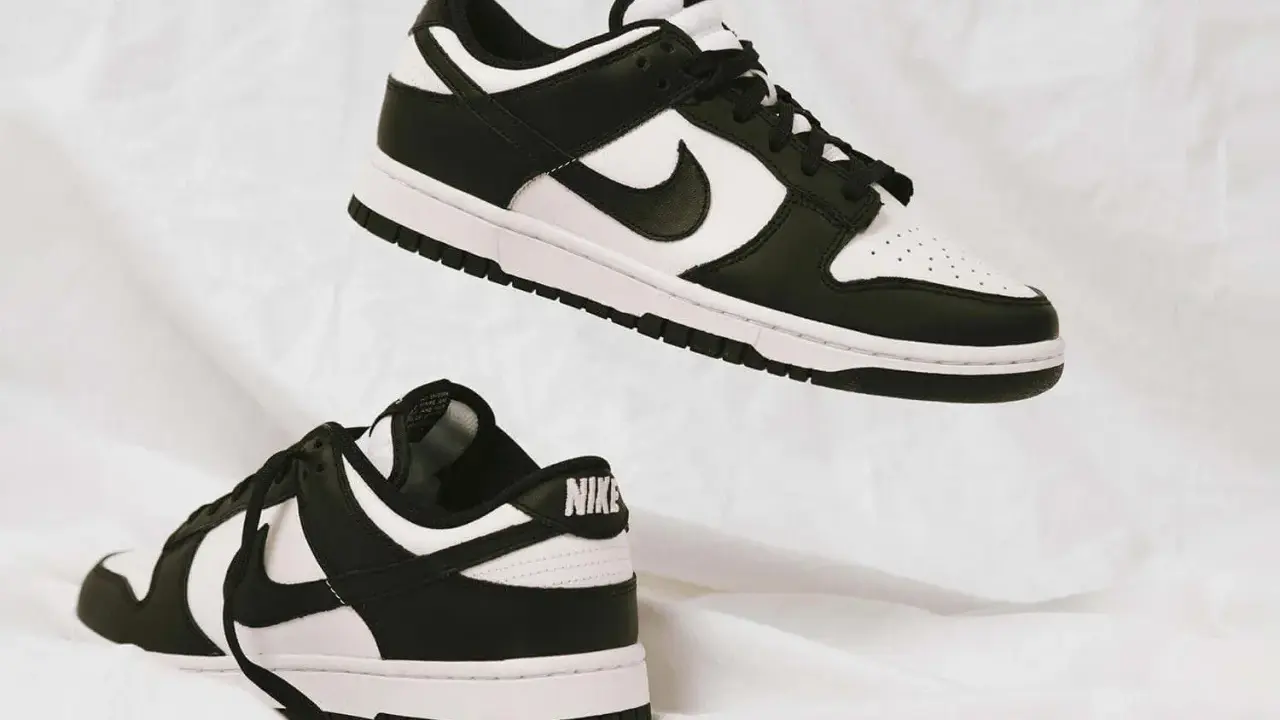 Zwei schwarz-weiße Nike Dunk Low Sneaker schweben auf weißem Stoff. Sie fallen größtenteils größengerecht aus.