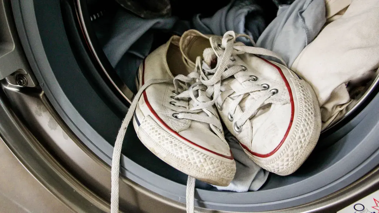 Weiße Turnschuhe mit roten Streifen liegen in einer Waschmaschine, bereit für die Reinigung.