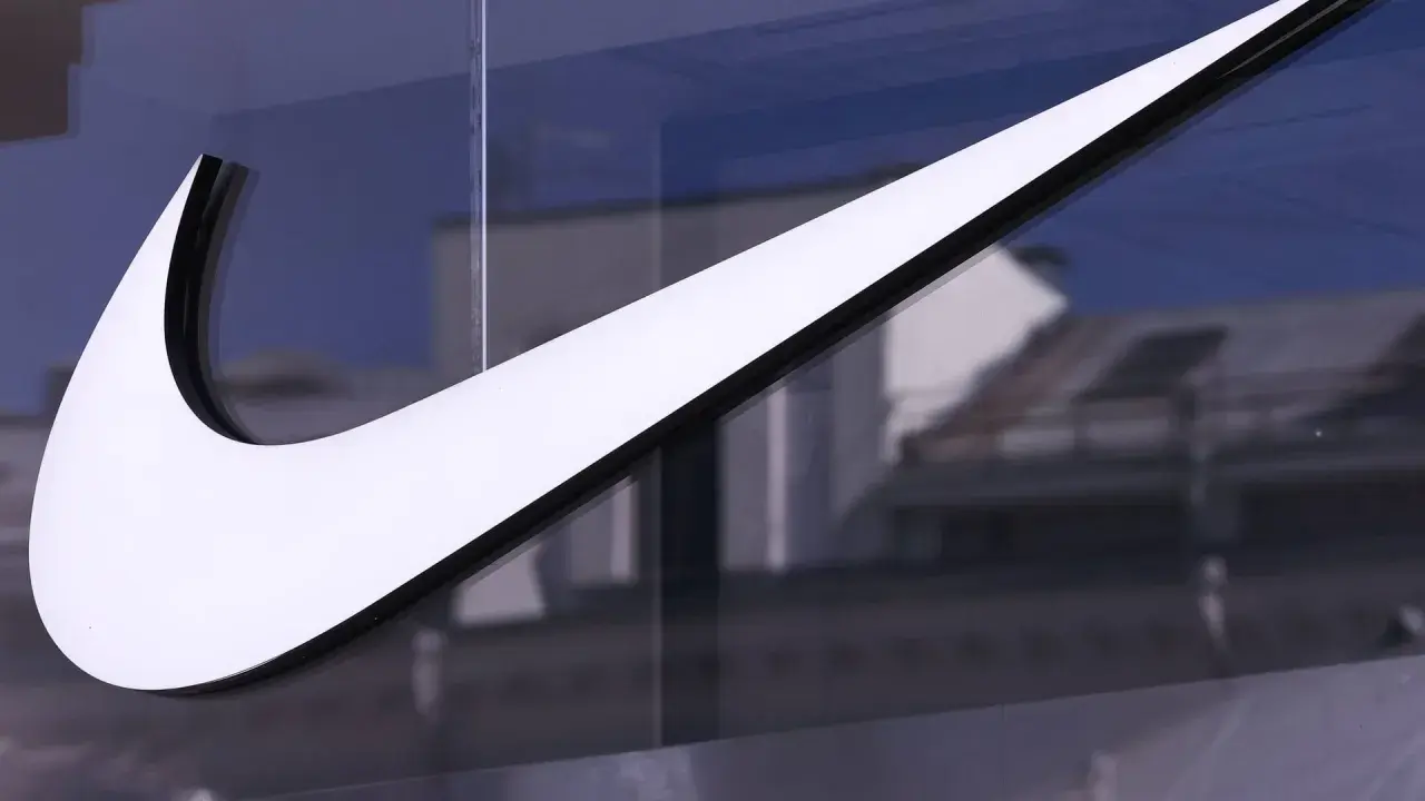 Großes, weißes Nike-Logo auf einer Glasfassade, reflektiert Gebäude im Hintergrund.