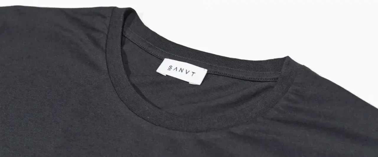 Dunkelgraues T-Shirt mit weißem Etikett "SANVT". Perfekt für den Sommer, ab 20 Grad tragbar.