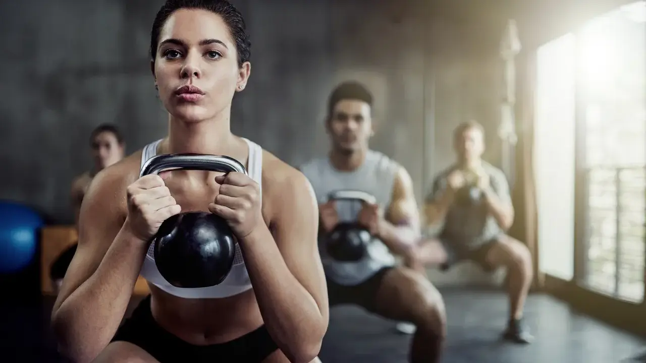 Frau führt Kettlebell-Squats aus, Teil einer intensiven Metcon-Trainingseinheit mit anderen Trainierenden im Hintergrund.