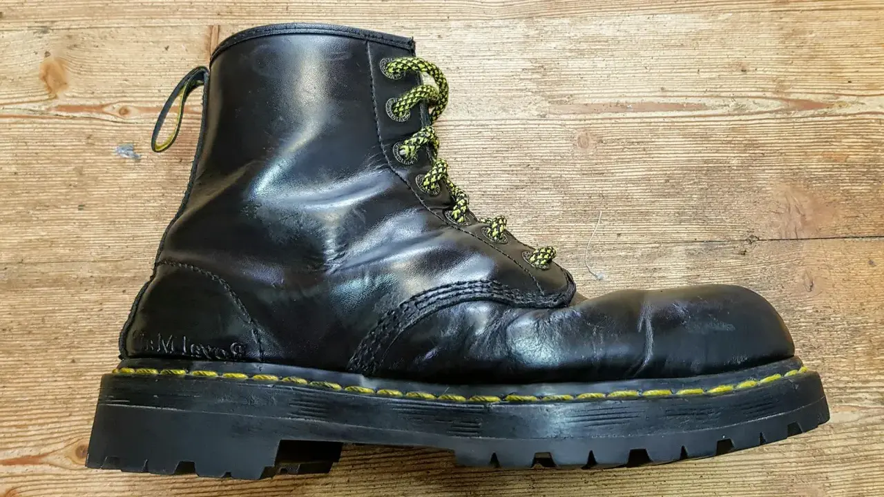 Schwarzer Dr. Martens Stiefel mit gelben Schnürsenkeln und einer neuen, robusten Sohle auf Holzuntergrund.