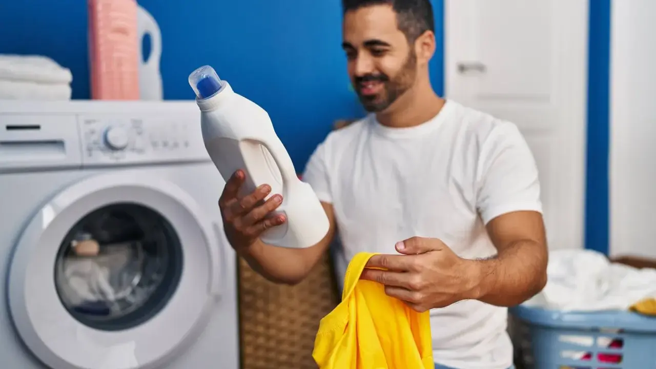 Mann hält Waschmittel und ein gelbes Trikot bereit, um die Wäsche zu waschen.