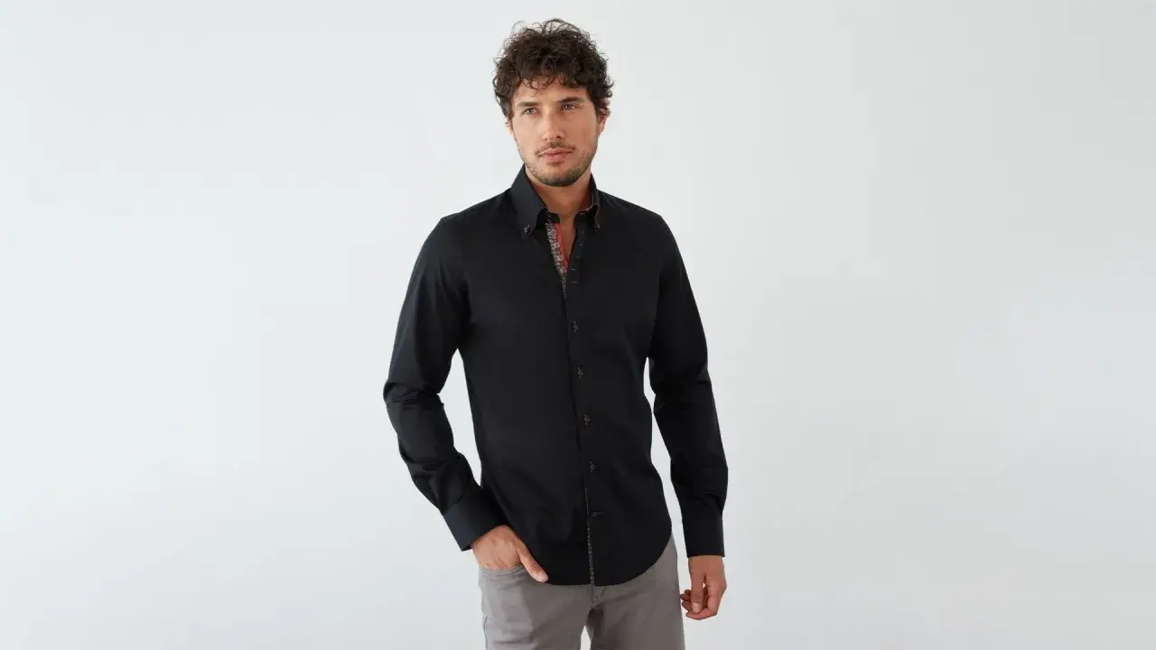 Mann in schwarzem Hemd mit farbigem Kragen und grauer Hose. Ein stilvoller Look, wie man ein schwarzes Hemd kombinieren kann.