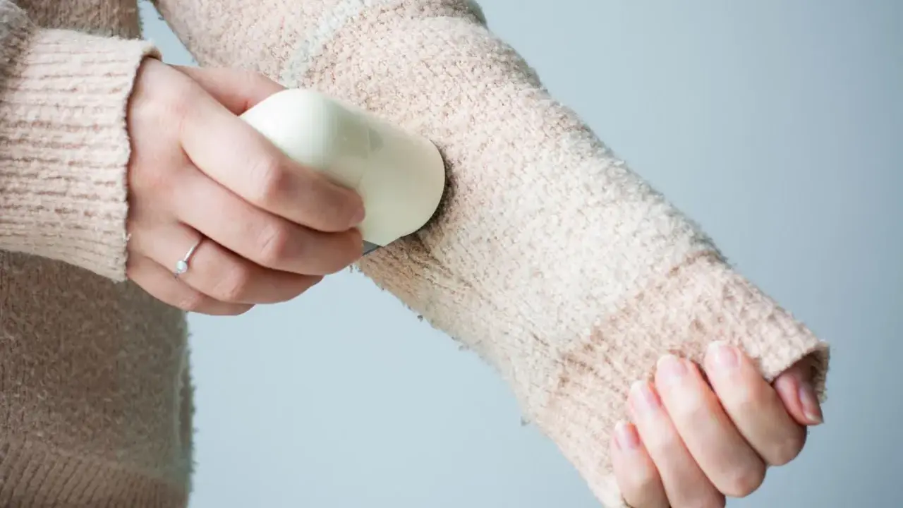 Frauenhand entfernt mit einem Hausmittel Fussel von einem Strickpullover.