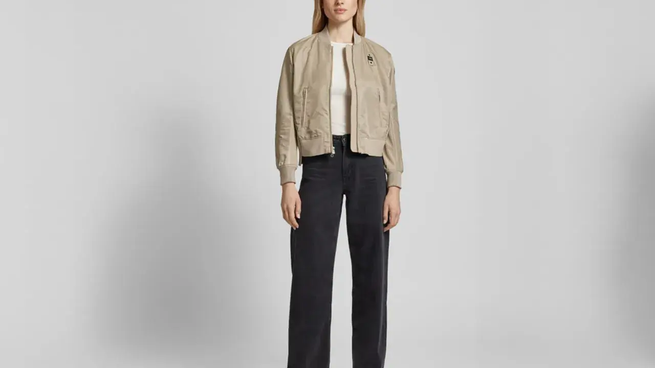 Frau stylt eine beige Bomberjacke mit weiten schwarzen Jeans und weißen Sneakern. Ein lässiger Look, der sich leicht anpassen lässt.