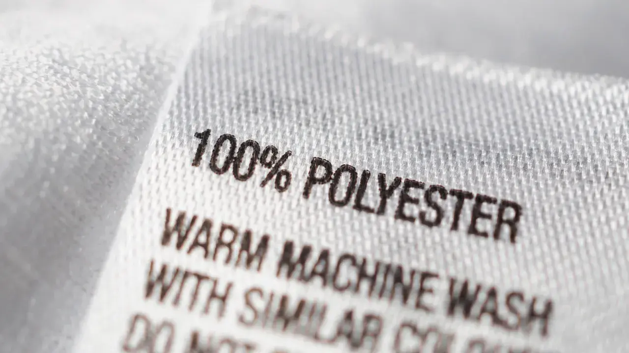 Etikett zeigt "100% POLYESTER". Pflegehinweise für das pflegeleichte Polyester-Material.