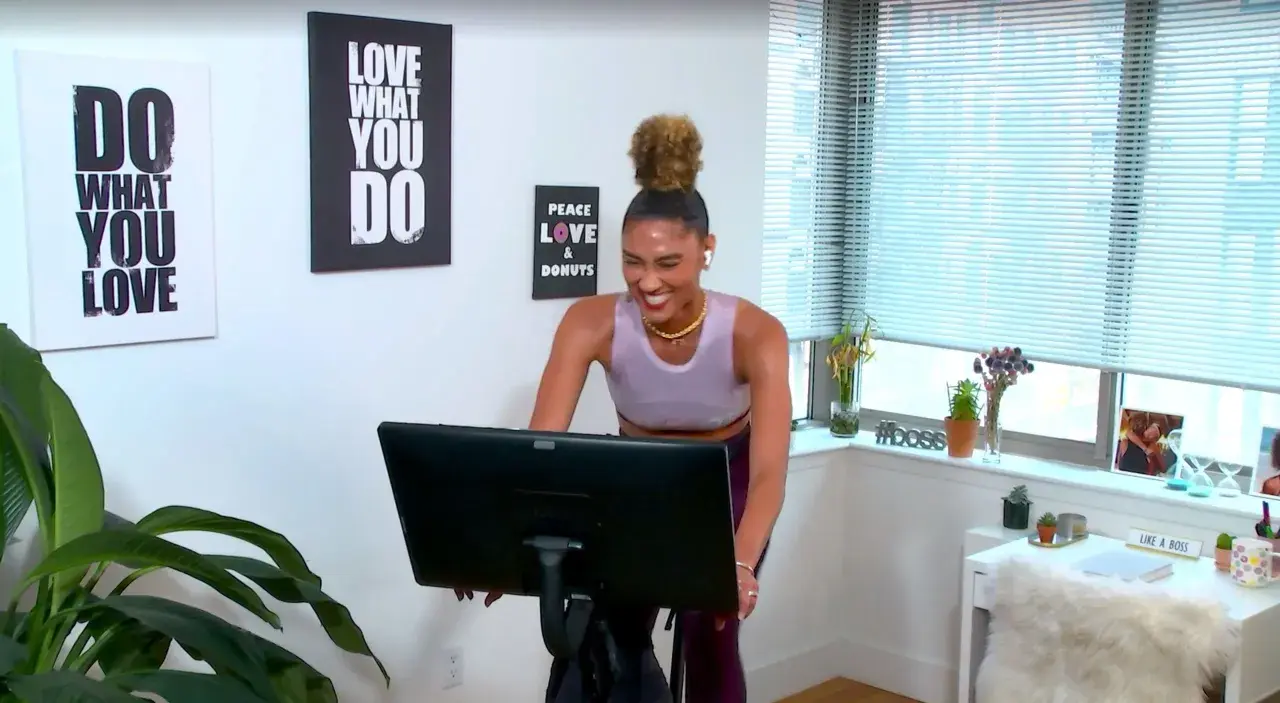 Frau lacht auf einem Heimtrainer, bereit für ein intensives Tabata Workout. Wandbilder motivieren: "Do what you love".