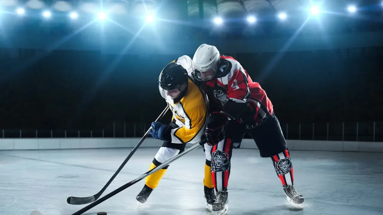 Zwei Eishockeyspieler im Kampf um den Puck. Perfekt, um zu sehen, was anziehen zum Eishockey gucken: warme Kleidung und gute Laune!