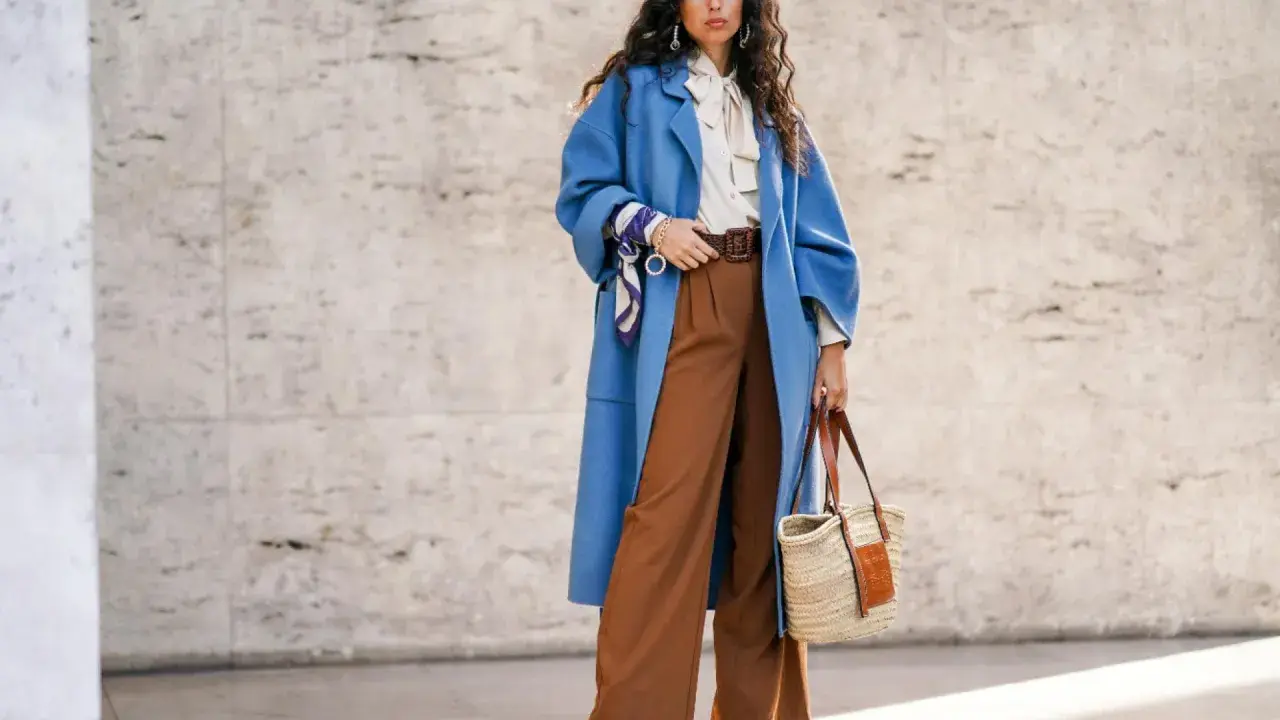 Stilvolles Outfit: Blaue Oversize-Jacke, cremefarbene Bluse mit Schleife und braune weite Hose kombinieren. Accessoires: Korbtasche, Gürtel, Halstuch.