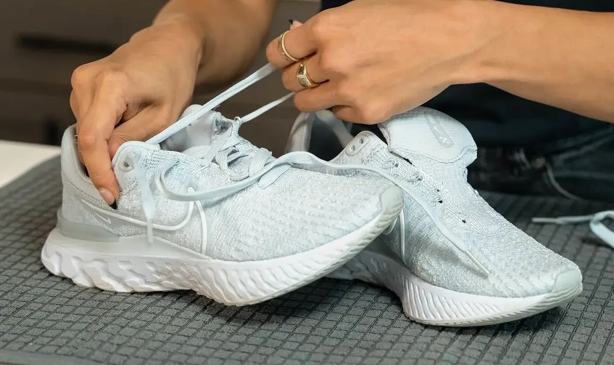Hände ziehen Schnürsenkel durch hellblaue Mesh Schuhe. So einfach lassen sich die Lieblingssneaker reinigen.