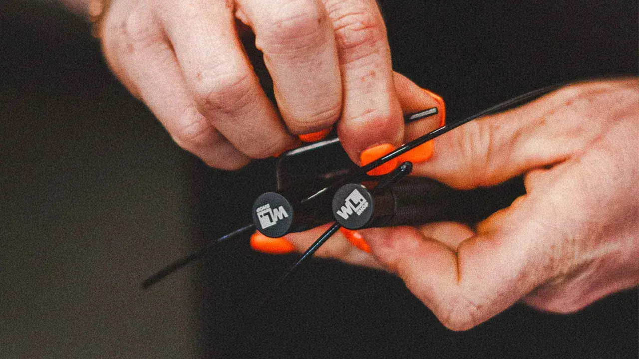 Hände mit orangen Nägeln stellen ein Springseil ein. Die Griffe haben ein Logo.