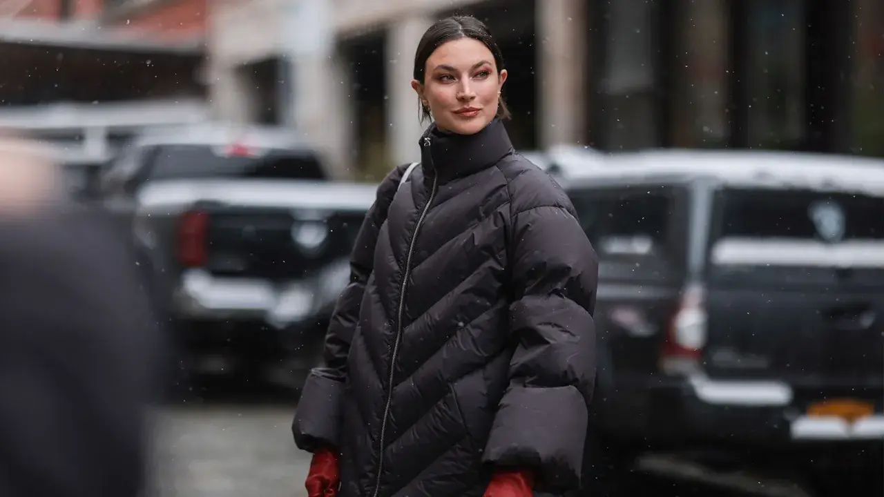 Frau in schwarzer Daunenjacke mit roten Handschuhen im Schnee. Für die Pflege der Daunenjacke im Trockner: welches Programm ist am besten?