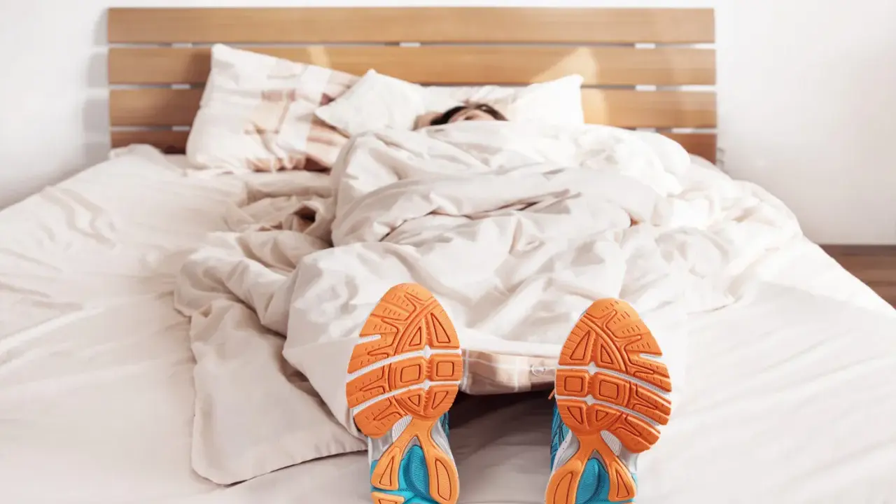 Füße mit Laufschuhen ragen aus einer Decke. Der Wecker klingelt, aber die Person träumt noch vom morgens joggen.
