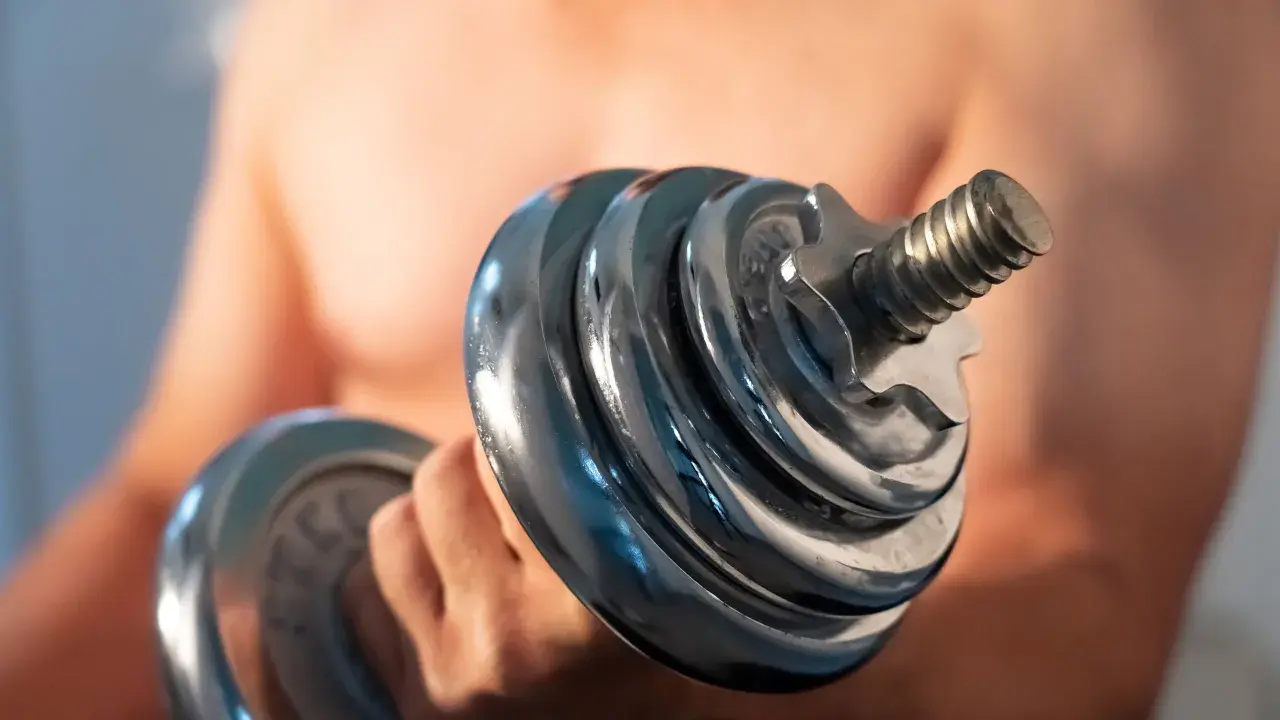 Mann hebt Hantel. Die Frage "wie lange dauert muskelaufbau" beschäftigt viele Fitnessbegeisterte.