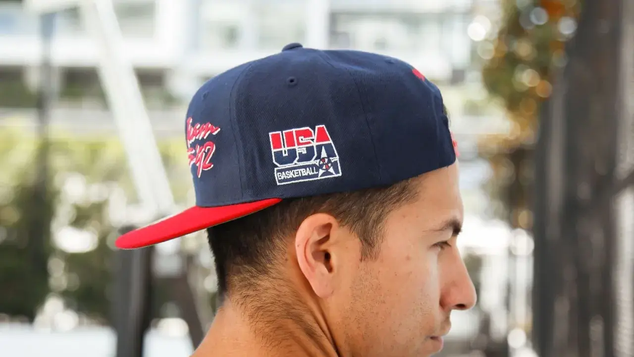 Junger Mann trägt eine dunkelblaue Kappe mit rotem Schirm und "USA Basketball"-Aufdruck, den **cap nach hinten tragen** ist sein Stil.