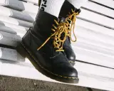 Schwarze Dr. Martens mit gelben Schnürsenkeln auf einer weißen Bank. Sie fallen eher groß aus, also lieber eine Nummer kleiner wählen.