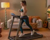 Frau macht Intervalltraining auf Laufband im Wohnzimmer. Sie trägt Sportkleidung und läuft mit Energie.
