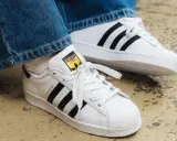 Weiße Adidas Superstar Sneaker mit schwarzen Streifen und gelbem Logo. Perfekt, um das Adidas modell herausfinden.