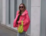 Stylische Frau in knallpinker Jacke und Sonnenbrille. Perfekt, um was anziehen bei 15 Grad. Dazu eine grüne Tasche.
