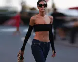 Frau in typischer 2000er Mode: schwarzer Bandeau-Top, tief sitzende Jeans und Armstulpen. Sie trägt Sonnenbrille und eine Tasche.
