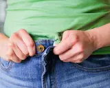 Hände ziehen am Bund einer Jeans, um sie weiter zu machen.