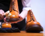 Hände bürsten braune Lederschuhe, um sie zu reinigen. Daneben steht eine Dose Schuhcreme.