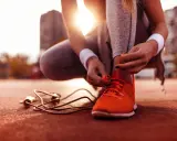 Sportlerin bindet ihre neuen, leuchtend orangen Laufschuhe ein. Die Sonne scheint, ein Springseil liegt bereit.