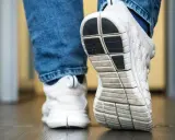 Weiße Turnschuhe mit Jeans. Die Sohle der Schuhe quietschen auf dem Boden, als jemand einen Schritt macht.
