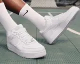 Weiße Nike Air Force 1 Sneaker mit schwarzen Socken auf einem grünen Untergrund. Perfekt zum Air Force 1 binden und loslegen.