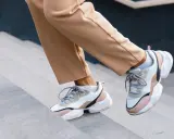 Schritte aufwärts in beigen Hosen und trendigen Sneakern mit sichtbaren Socken. Der socken in sneaker trend ist hier perfekt umgesetzt.