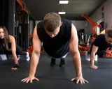 Drei Personen machen Liegestütze im Fitnessstudio. Sie lernen, was sind Burpees, eine Ganzkörperübung.