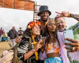 Bunte Outfits, Blumenkränze und Peace-Zeichen: So zieht man zu einem Rave an! Vier Freunde machen ein Selfie.