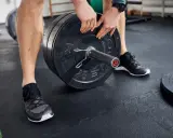 Mann lädt Gewichtsscheiben auf eine Langhantel in einem Fitnessstudio.