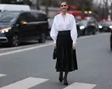 Chic Frau in weißer Bluse und schwarzem oberteil zu plisseerock, steht auf Zebrastreifen.