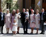 Familie in festlicher Kleidung, die überlegt, was anziehen zur Taufe. Ein Mann trägt ein Baby, Kinder und Frauen in eleganten Kleidern.