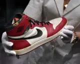 Ein Paar abgenutzte Air Jordan 1 Sneaker, die seit 1985 erhältlich sind, werden von einer Person mit weißen Handschuhen gehalten.