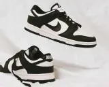 Zwei schwarz-weiße Nike Dunk Low Sneaker schweben auf weißem Stoff. Sie fallen größtenteils größengerecht aus.